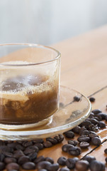 Hot coffee in glass cups and coffee beans on a wooden table.