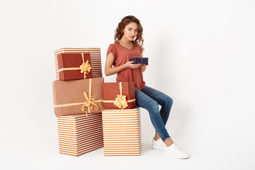 Young beautiful girl sitting on big gift box holding smaller one in hands Isolated