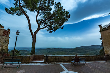 Loneliness
Man alone is relaxing on a green wooden bench with a great view in a small town in Italy. There is tree, scenery landscape, two benches, two street lamps and walls. Tuscany region.
