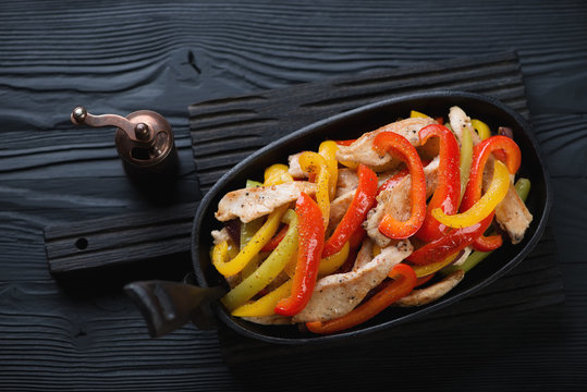 Frying pan with fajitas on a black wooden background, above view