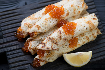 Close-up of rolled crepes with red caviar and lemon, studio shot