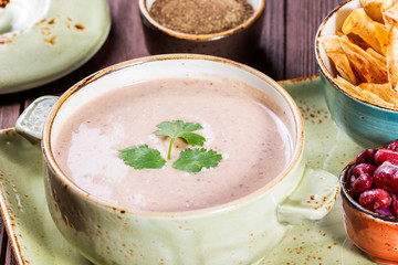 Cream soup with beans, vegetables, herbs and crackers on plate on dark wooden background. Homemade food. Ingredients on table