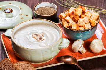 Cream soup with mushrooms, herbs, cream and crackers on plate on dark wooden background. Homemade food. Ingredients on table. Top view