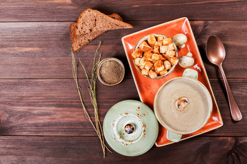 Cream soup with mushrooms, herbs, cream and crackers on plate on dark wooden background. Homemade food. Ingredients on table. Top view