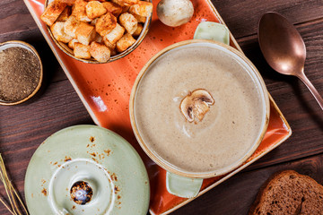 Cream soup with mushrooms, herbs, cream and crackers on plate on dark wooden background. Homemade food. Ingredients on table. Top view