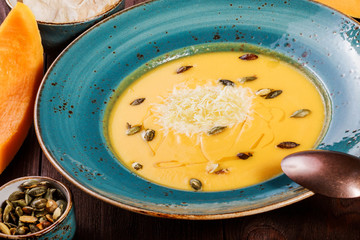 Pumpkin and carrot soup with parmesan cheese, pumpkin seeds and bread on dark wooden background. Ingredients on table.Top view
