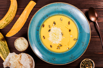 Pumpkin and carrot soup with parmesan cheese, pumpkin seeds and bread on dark wooden background. Ingredients on table.Top view