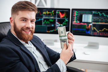 Cheerful bearded young businessman sitting and holding dollars