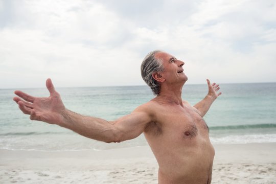 Happy senior man standing on beach with arms outstretched