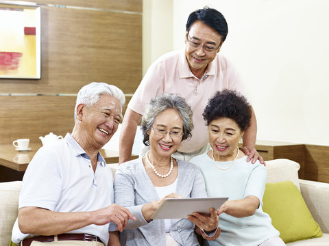two happy senior asian couples using tablet computer at home