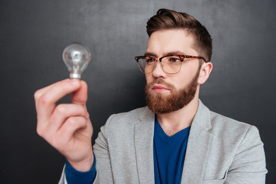 Serious bearded young businessman standing and looking at light bulb