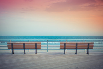 pastel toned beach boardwalk benches with ocean and sunset - obrazy, fototapety, plakaty
