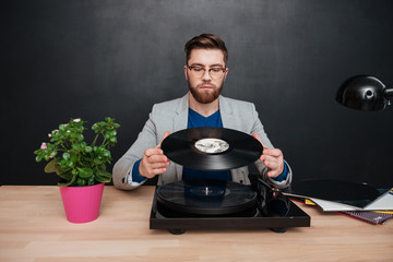 Handsome bearded businessman in glasses using turntable and vinyl record
