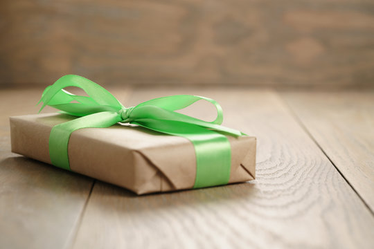 rustic craft paper gift box with green ribbon bow on wood table, shallow focus