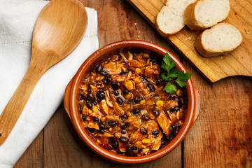 Gusio de alubias negras con salsa dentro de un cuenco junto a unas rodas de pan sobre una tabla de madera rústica. Vista superior y de cerca