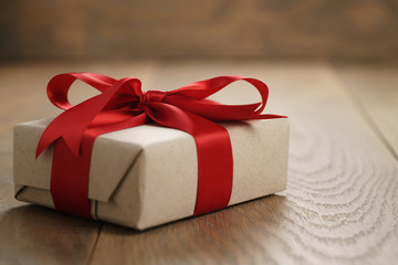 rustic craft paper gift box with red ribbon bow on wood table, shallow focus