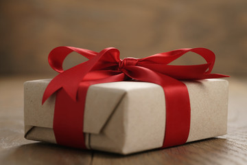 rustic craft paper gift box with red ribbon bow on wood table, shallow focus
