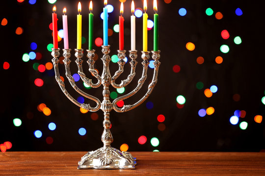 Menorah with candles for Hanukkah on wooden table against defocused lights