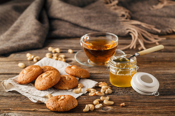 Oatmeal cookies with nut, jar with honey  on napkin on brown woo
