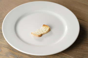 white plate with single dry slice of baguette bread, focus on bread