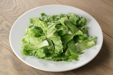 torn romaine lettuce leaves in plate on wood table, diet food