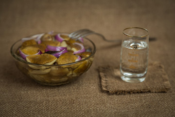 Vodka and a snack of pickled mushrooms on brown background
