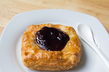 Danish blueberry pie with spoon in white plate on wooden table