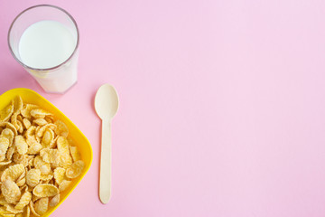 Bowl and spoon with corn flakes on  pink background
