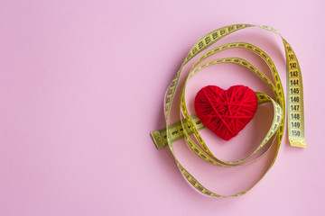Red heart with yellow tape measure on  pink background