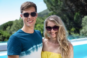 Happy couple in sunglasses standing near the pool