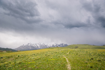 Fototapeta na wymiar Mountain peaks with snow and green pastures under dark cloudy sky in the At Bashi, Kyrgyzstan
