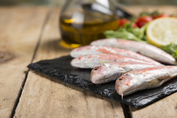 raw red mullet served on curly salad on slate plate on wooden table