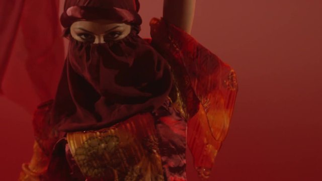 Beautiful traditional oriental belly dancer. Oriental girl dancing on red background. Studio shoot with fire. Shot on RED EPIC DRAGON Cinema Camera in slow motion.