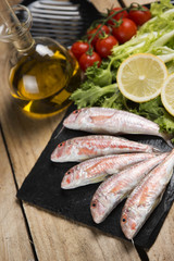 raw red mullet served on curly salad on slate plate on wooden table