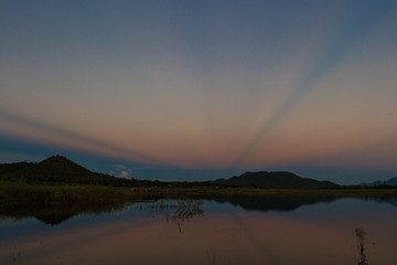 Sunset in twilight time behind the mountains front water of a reservoir with copy space.