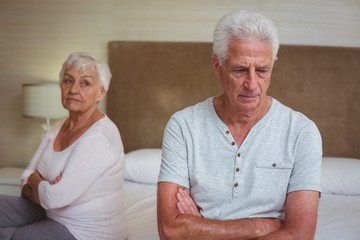 Unhappy senior couple after arguing while sitting on bed 