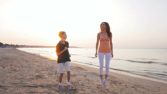 Mother and her sun doing sport exercises on the beach at sunset or sunrise, slow motion