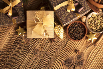 Christmas theme, christmas decoration. presents in boxes on a wooden table with golden baubles, clove, cardamon, star anise, cinnamon. Golden and brownish aesthetics. Place for typography and logo.
