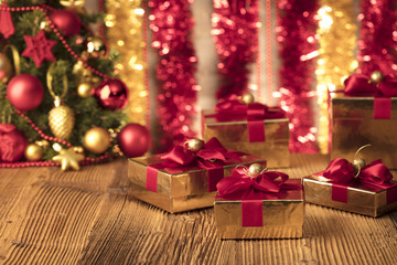Golden presents with red ribbon under christmas tree. Wooden background and table. Red and gold. Place for typography and logo. Copy space.