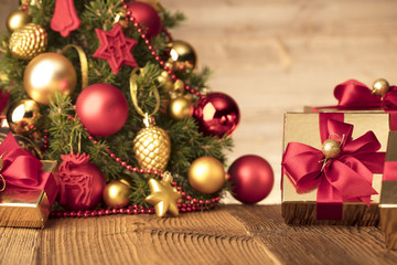 Golden presents with red ribbon under christmas tree. Wooden background and table. Red and gold. Place for typography and logo. Copy space.