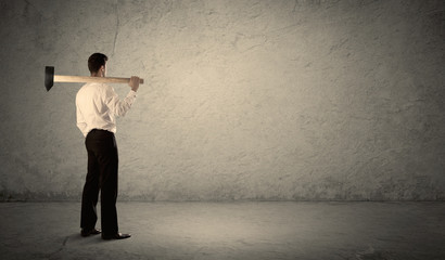 Business man standing in front of a grungy wall with a hammer