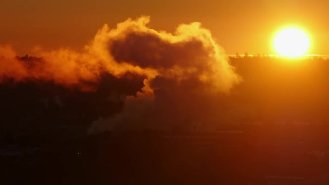 Industrial Pollution fills the sky as the sun comes up behind a factory. HD Zoom Out.