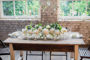 Loft style wedding table decorated with white rare David Austin roses. Beutiful rustic wedding decoration. Candles in glass holders. Nice romantic flowers.