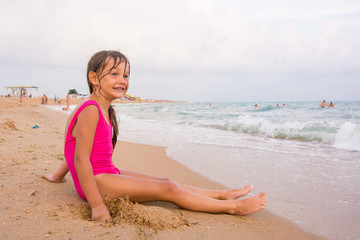 Fototapeta na wymiar Five-year girl sits on a beach and seaside fun looking into the distance