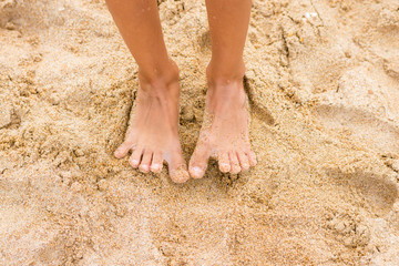 Fototapeta na wymiar Legs slender seven-year girl standing barefoot on the sand
