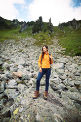 Obraz premium Young woman traveler with backpack relaxing outdoor with rocky mountains on background. Lifestyle hiking concept. Backpacker hiking at mountain peak