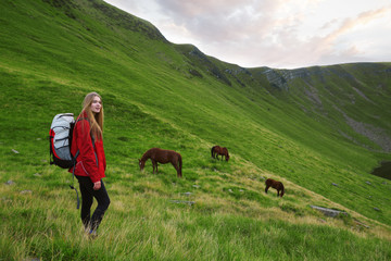Portrait of a beautiful young woman looking at the landscape while hiking in a mountains with horses in the background