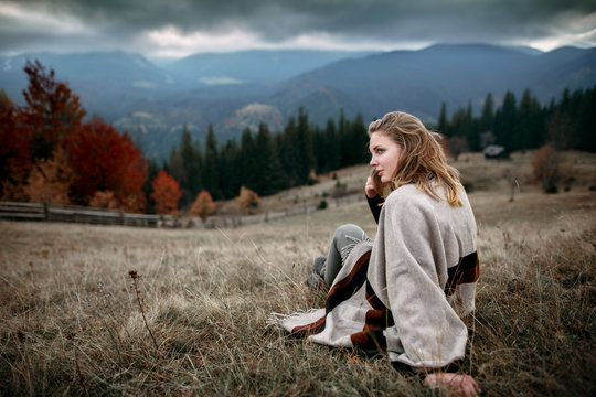 Woman in boho style. Hiker girl wrapping in warm poncho outdoor. Shot of a young woman looking at the landscape while hiking in the mountains.Outdoor shot of attractive young woman