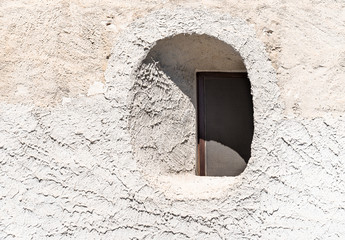 Little round window inside the stone wall of the old typical mediterranean house in Sicily.