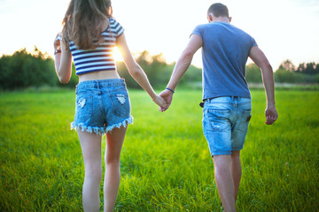 Rear view shot of young woman walking with her boyfriend on grass field